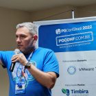 Emanuel Araujo Carneiro palestrando na PGConf Brasil 2022, sobre a resiliência de Rocky Balboa. Homem branco com microfone em sala de conferência.