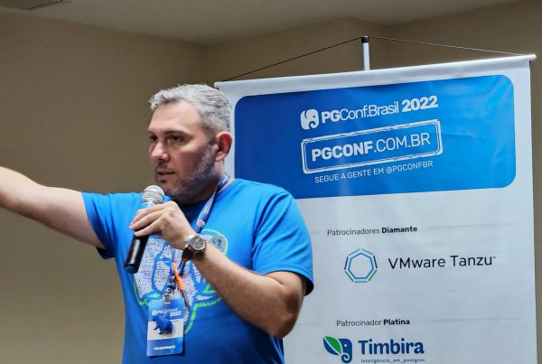 Emanuel Araujo Carneiro palestrando na PGConf Brasil 2022, sobre a resiliência de Rocky Balboa. Homem branco com microfone em sala de conferência.