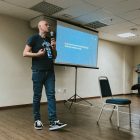 Dickson Guedes, consultor da Timbira, palestrando na PGConf.Brasil 2022. Ele segura um microfone enquanto apresenta sobre automação com SQL para uma plateia.