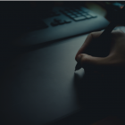 Mesa com teclado de notebook, mão segurando uma caneta, simbolizando análise e avaliação de banco de dados PostgreSQL.